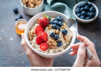 Oatmeal Porridge Bowl With Berry Fruits In Female Hands, Closeup View. Healthy Vegetarian Breakfast Food