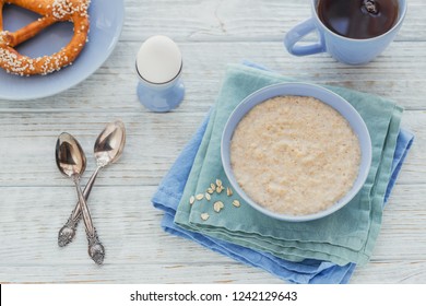 Oatmeal Porridge Bowl With Black Tea, Bread And Boiled Egg On The White Wooden Background. Healthy Nutritious Breakfast. Concept Of Healthy Eating, Dieting. Top View