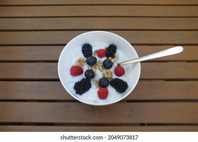 Oatmeal porridge bowl with blackberries, raspberries, blueberries and walnuts on a brown wooden table