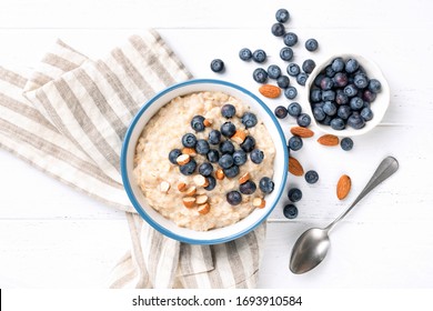 Oatmeal porridge in a bowl with fresh blueberries and almond nuts on a white wooden table. Top view. Healthy breakfast food - Powered by Shutterstock