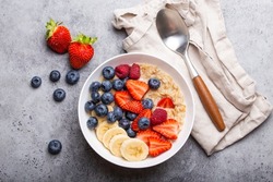 Oatmeal Porridge With Fruit And Berries In Bowl With Spoon On White Wooden Background Table Top View, Homemade Healthy Breakfast Cereal With Strawberry, Banana, Blueberry, Raspberry