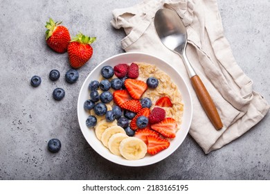 Oatmeal Porridge With Fruit And Berries In Bowl With Spoon On White Wooden Background Table Top View, Homemade Healthy Breakfast Cereal With Strawberry, Banana, Blueberry, Raspberry