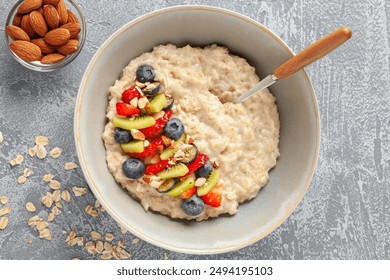 Oatmeal porridge with fruit and berries in bowl on the table. Homemade healthy breakfast cereal with strawberry, kiwi fruits, blueberry and almond. Top view - Powered by Shutterstock