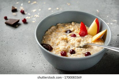 oatmeal porridge with pieces of fruit, pear, berries, orange, on a gray background - Shutterstock ID 1700083369