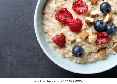 Oatmeal porridge with raspberries, blueberries and  almonds in bowl on black background - Powered by Shutterstock