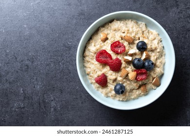 Oatmeal porridge with raspberries, blueberries and  almonds in bowl on black background. Top view. Copy space