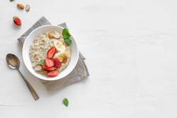 Oatmeal Porridge With Strawberries, Almonds And Banana In White Bowl. Healthy Breakfast With Oatmeal And Fresh Organic Berries, Top View, Copy Space.