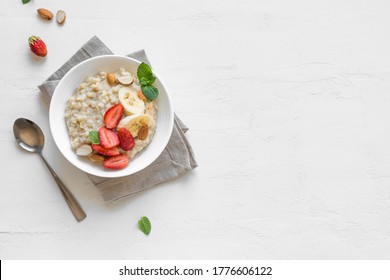 Oatmeal Porridge with Strawberries, Almonds and Banana in white bowl. Healthy Breakfast with Oatmeal and Fresh Organic Berries, top view, copy space. - Shutterstock ID 1776606122