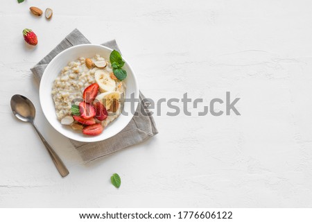 Oatmeal Porridge with Strawberries, Almonds and Banana in white bowl. Healthy Breakfast with Oatmeal and Fresh Organic Berries, top view, copy space.