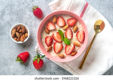 oatmeal porridge with strawberries, almonds, mint leaf in pink bowl, spoon and napkin with red stripes on concrete background Top view Flat lay Vegan food concept Healthy breakfast