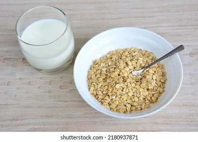 oatmeal in the white bowl with spoon and glass of milk on beige background