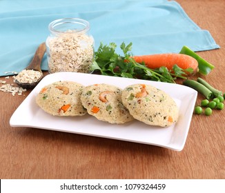 Oats Idli Or Cake, A Healthy Indian Vegetarian Steam-cooked Food, With Vegetables Like Carrot And Peas,  On A Ceramic Tray.