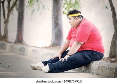 obese man looks tired after exercising in the park while sitting on the road at autumn time