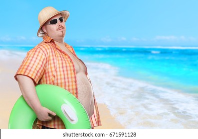 Obese man in swimsuit with green lifebuoy. Holidays on the beach.Funny tourist sending greeting from tropical paradise.