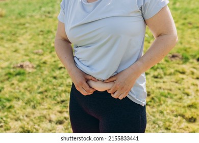 Obese woman hand holding excessive belly fat over nature background. Diet concept to reduce belly and shape up healthy stomach muscle, close up