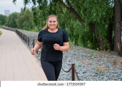 Eine fettleibige junge Frau joggt draußen. Fat schöne lächelnde Mädchen in einem schwarzen Tracksuit ist in Fitness für Gewichtsverlust auf der Wasserfront engagiert. Eine Frau läuft an einem Sommertag.