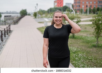 An obese young woman jogging outdoors. Fat beautiful smiling girl in a black tracksuit is engaged in fitness for weight loss on the waterfront. A woman runs on a summer day. - Shutterstock ID 1888316032