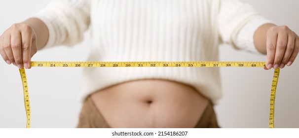 An Obesity Using Measuring Tape To Show The Real Size. Chubby Fat Woman Using Measure Tape At Belly. Real Size Woman After Gave Birth To Baby, Real Skin With Wrinkles And Scars. 