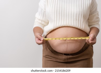 An Obesity Using Measuring Tape To Show The Real Size. Chubby Fat Woman Using Measure Tape At Belly. Real Size Woman After Gave Birth To Baby, Real Skin With Wrinkles And Scars. 