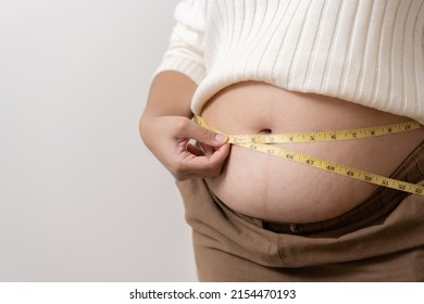 An Obesity Using Measuring Tape To Show The Real Size. Chubby Fat Woman Using Measure Tape At Belly. Real Size Woman After Gave Birth To Baby, Real Skin With Wrinkles And Scars. 