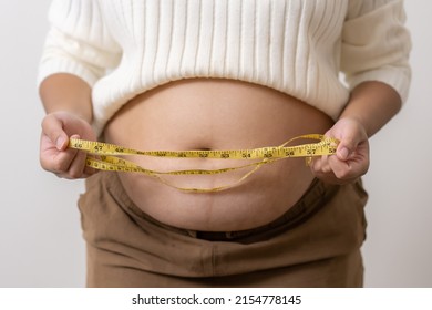 An Obesity Using Measuring Tape To Show The Real Size. Chubby Fat Woman Using Measure Tape At Belly. Real Size Woman After Gave Birth To Baby, Real Skin With Wrinkles And Scars. 