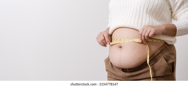 An Obesity Using Measuring Tape To Show The Real Size. Chubby Fat Woman Using Measure Tape At Belly. Real Size Woman After Gave Birth To Baby, Real Skin With Wrinkles And Scars. 