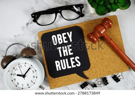 Obey The Rules text on speech bubble with alarm clock and wooden gavel on marble background