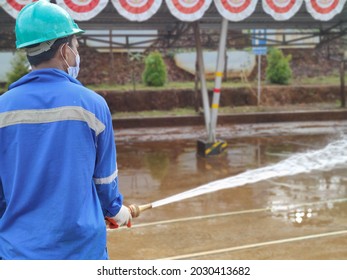 Obi, Indonesia: August 16, 2021, The Environment Crew Is Flushing The Field From The Mud Using A Hydrant Hose, Seen Wearing Masks And Helmets.