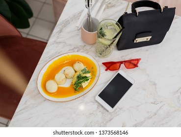 Object composition on marble table. Breakfast in cafe.  Tasty cheesecakes and fresh lemonade.   Mobile phone and black leather bag. Top view.