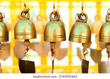 Object Series : Traditional brass bells hanging in a row at a Thai Buddhist temple. These sacred symbols represent the belief in gaining good luck and widespread fame through merit making. The gentle sound creates a peaceful atmosphere reflecting longstanding spiritual culture.