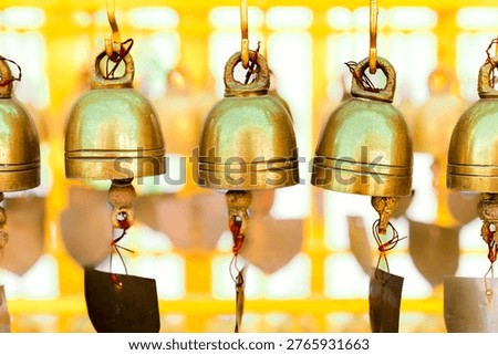 Object Series : Traditional brass bells hanging in a row at a Thai Buddhist temple. These sacred symbols represent the belief in gaining good luck and widespread fame through merit making. The gentle sound creates a peaceful atmosphere reflecting longstanding spiritual culture.