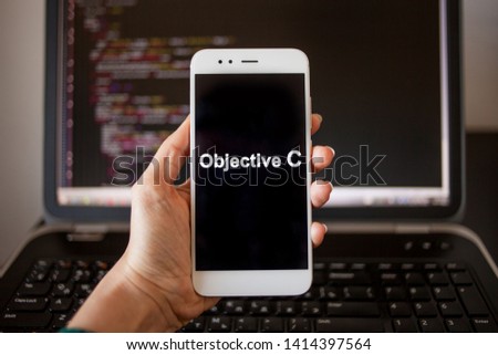 Objective C Mobile application development, programming language for mobile development. Smartphone in hand with the inscription Objective C on the screen