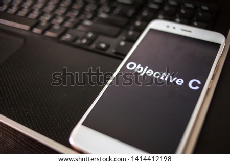 Objective C Programming language for mobile development, concept. Smartphone on the laptop keyboard, the programmer's workplace