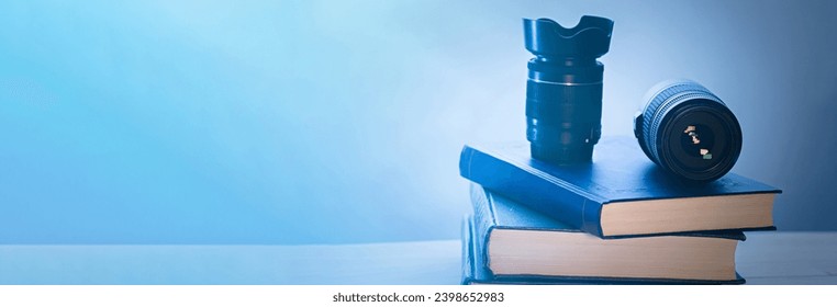 Objective of a camera and a stack of books on a wooden board