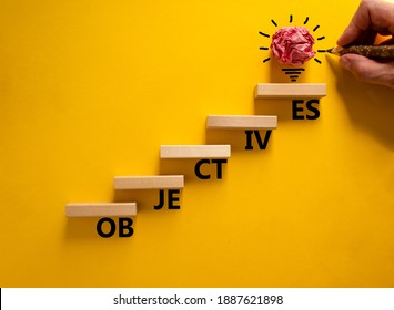 Objectives symbol. Wood blocks stacking as step stair on yellow background, copy space. Businessman hand and light bulb. Word 'Objectives'. Business and objectives concept.