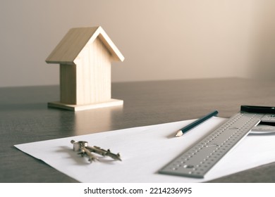 Objects on the table in an architect's office with a small wooden house in the background for decoration. - Shutterstock ID 2214236995
