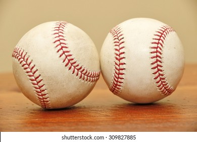 Objects: Two Baseballs On A Wood Table Touching Each Other.