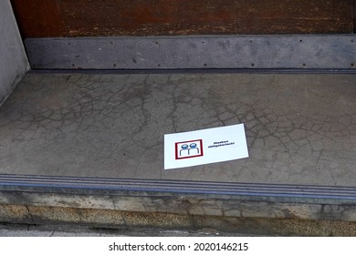 Obligatory Face Mask Sign With Inscription In German Language. There Is A Pictogram Of Two Persons Wearing Face Masks. The Sign Is Randomly On The Ground Of A Building.