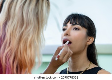 Oblique Angle Selective Focus Of A Young Beautiful Caucasian Model With Bangs Sitting Getting Make-up By A Professional Female Make-up Artist Using A Lip Liner Pencil Drawing The Contour To Her Lips.