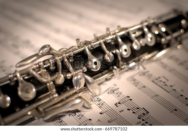 Oboe resting\
atop sheet music. The middle of the instrument appears in focus\
upon an open book of musical notes. The oboe has a black body with\
silver keys, made from grenadilla\
wood.