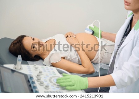 Obscure face of gynecologist doing ultrasound examination of pregnant woman