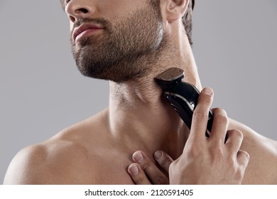 Obscure face of young man shaving beard with electric razor. Handsome dark-haired bearded guy. Concept of face care. Idea of male beauty. Isolated on white background. Studio shoot - Shutterstock ID 2120591405