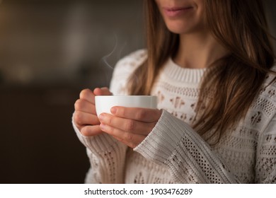 Obscured young woman drinking hot tea or coffee and smiling
