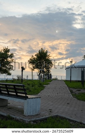 Observation deck with a bench and walking areas, trees and a tent. Cloudy sky and sunset. Summer evening. Ufa, Bashkiria