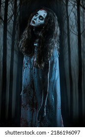 Obsessed Woman With Faded Eyes And Shaggy Black Hair Standing In A Bloody Nightie In The Dark Forest At Night. Zombie Woman. Horror, Thriller. Halloween. 