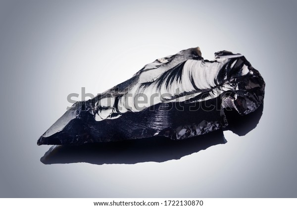 Obsidian stone arrowhead on black background\
with reflection