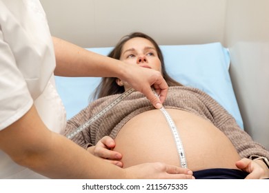 Obstetrician gynecologist measures a pregnant woman's belly with a measuring tape in medical office.Concept of pregnancy, prenatal care, medicine and healthcare.Selective focus.