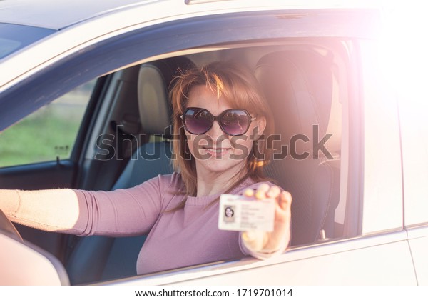 Obtaining a driver’s license, a\
beautiful woman in sunglasses at the wheel demonstrates a new\
driver’s license. Young woman holding a driver’s license near an\
open car.