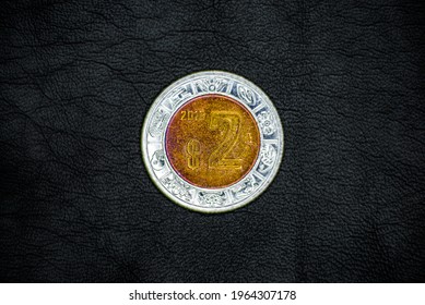 Obverse of used and old Mexican 2(two) pesos coin, minted in 2018, on black leather background. Stylized image of the “Ring of the Days of the Sun Stone.”