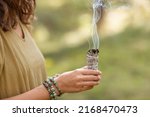 occult science and supernatural concept - close up of woman or witch with smoking white sage performing magic ritual in forest